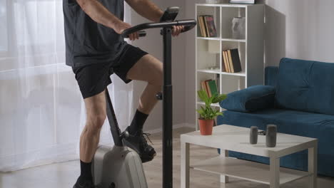 training-with-stationary-bicycle-in-home-conditions-man-is-spinning-pedals-in-living-room-workout-for-keeping-fit-and-health